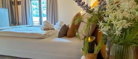 Un dormitorio con una cama, almohadas, un jarrón con flores y una ventana con cortinas.