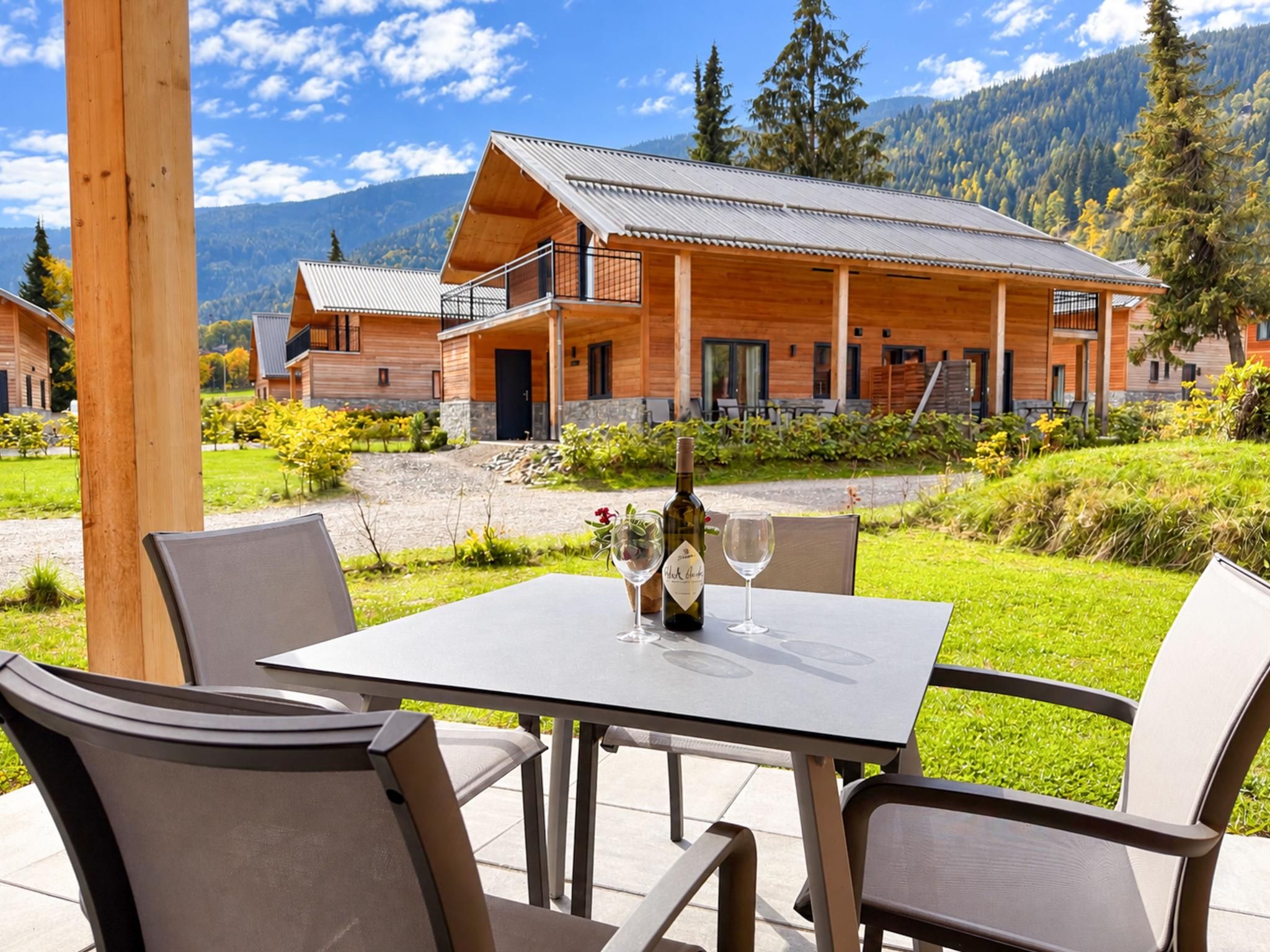 A wooden lodge with a balcony, a table with chairs, and a bottle of wine.