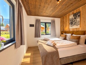 Ein Schlafzimmer mit einem Bett, Vorhängen, einem Fenster und einer Holzbalkendecke.