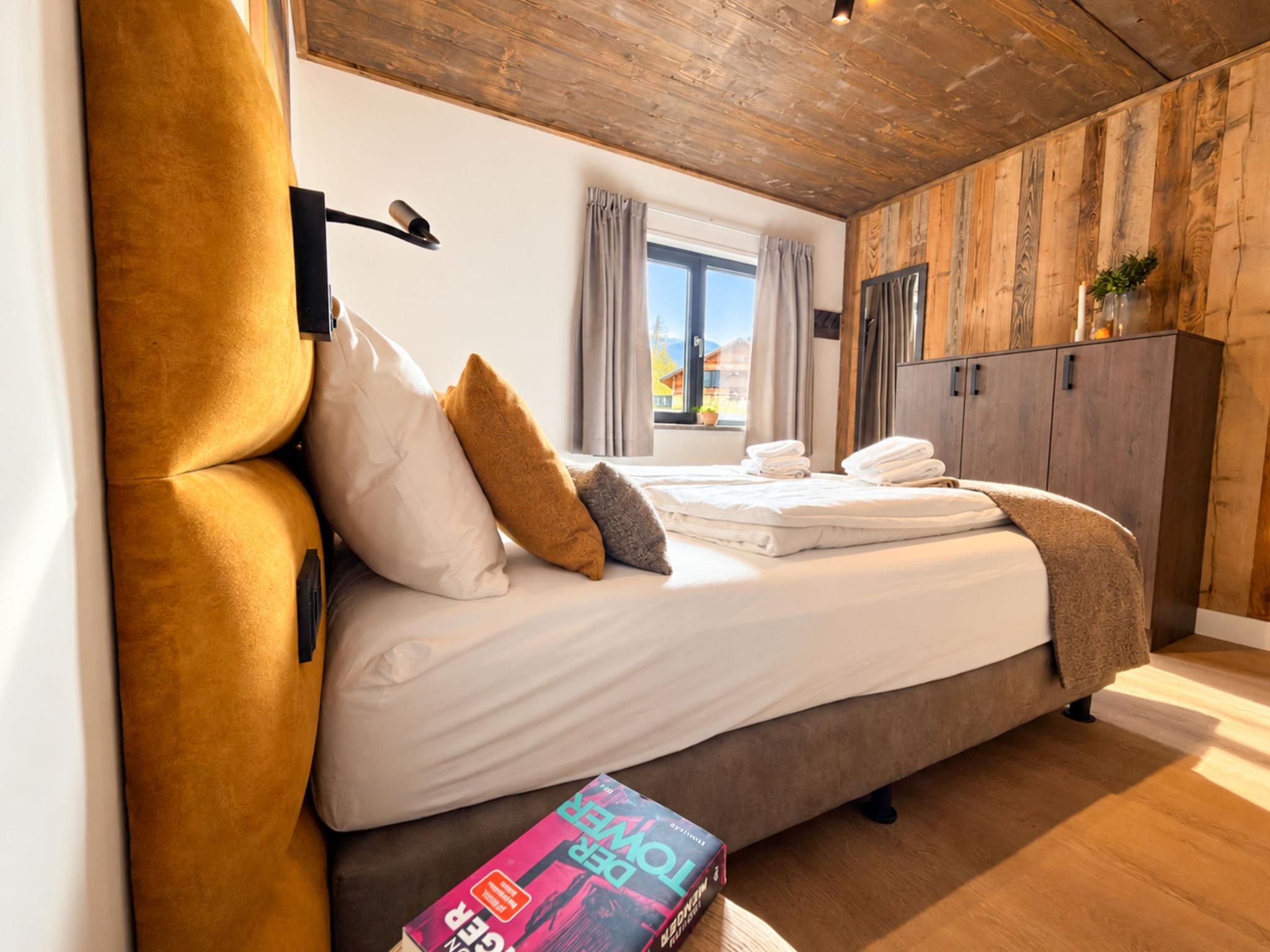 A bedroom with a bed, pillows, a bedside table, a window, and a wardrobe.