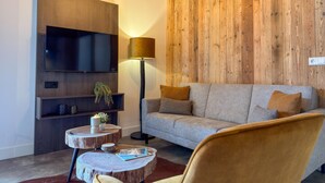 Ein modernes Wohnzimmer mit Flachbildfernseher, einer Couch, einer Lampe und einem runden Couchtisch.