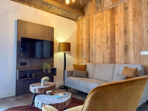 Een moderne woonkamer met een flatscreen televisie, een bank, een lamp en een ronde houten salontafel.