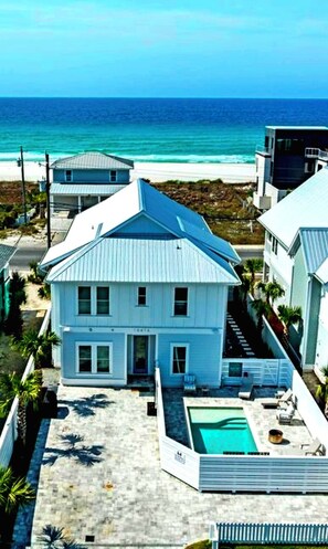 Ein zweistöckiges Haus mit Swimmingpool in Strandnähe, im Hintergrund der Ozean.