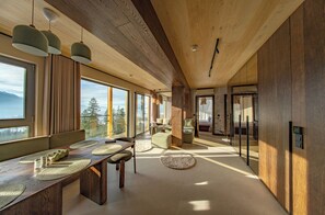 A modern interior with a wooden ceiling, large windows, and a dining area with a long table.