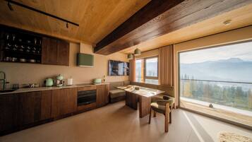 A modern kitchen with wooden cabinets, a dining area with a table and chairs, and a large window offering a mountain view.