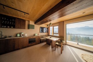 Een moderne keuken met houten kastjes, een eethoek met een tafel en stoelen, en een groot raam met uitzicht op de bergen.