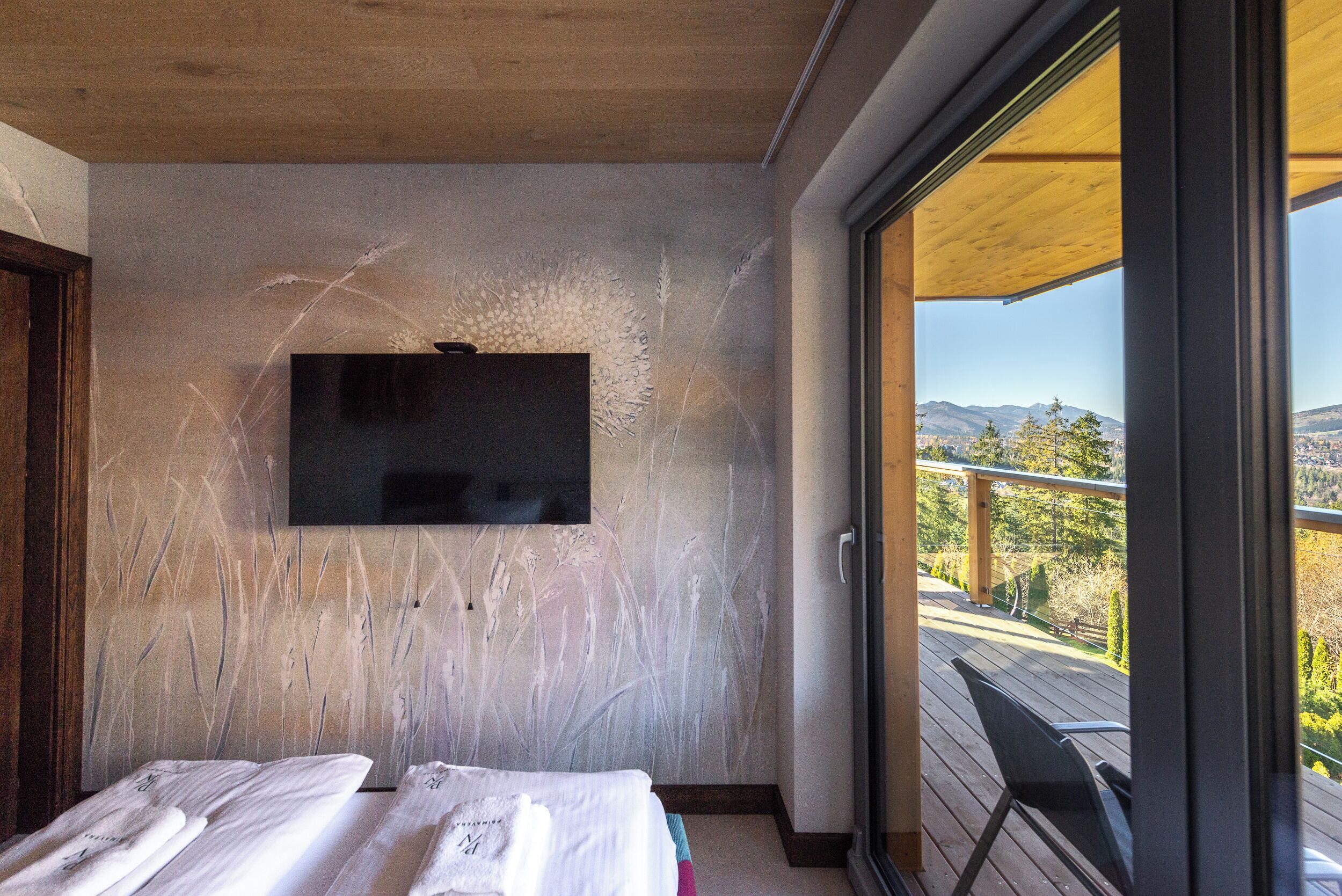 Una habitación con cama, televisión de pantalla plana en la pared y balcón con vistas al paisaje.