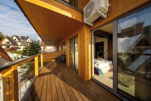 A wooden deck with a glass door leading to a bedroom with a bed and a suitcase. - Apartament Primavera (zakopane)