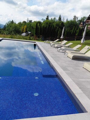 A swimming pool with a tiled edge and lounge chairs along the side. - Apartament Primavera (zakopane)