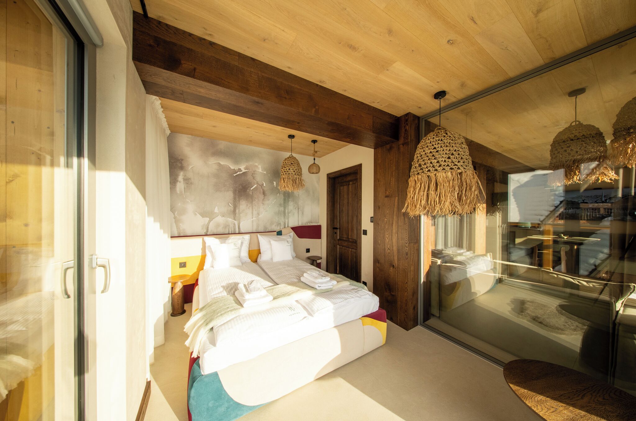 A modern bedroom with a large bed, wooden ceiling beams, and a glass door leading to a balcony.