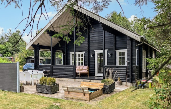 A black wooden cabin with a porch, outdoor seating, and potted plants. - Stunning home in Løgstør with WiFi (Løgstør)