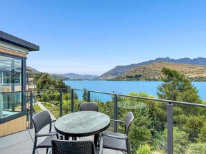 Ein Balkon mit rundem Tisch und Stühlen, mit Blick auf einen See und Berge.
