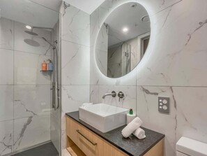 Ein modernes Badezimmer mit Marmorfliesen, einem weißen Waschbecken, einem Spiegel und einer Duschkabine.