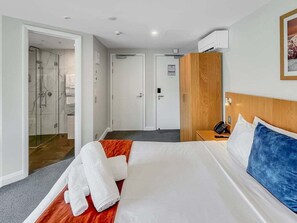 Ein Hotelzimmer mit Bett, Holz-Kopfteil, Schreibtisch mit Telefon und Duschbereich.