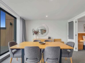 Ein moderner Essbereich mit Holztisch und grau gepolsterten Stühlen, einem runden Spiegel an der Wand und Blick auf einen Balkon.