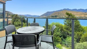 Um terraço com uma mesa redonda e cadeiras, com vista para um lago e montanhas.