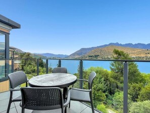 Eine Terrasse mit rundem Tisch und Stühlen, mit Blick auf einen See und Berge.