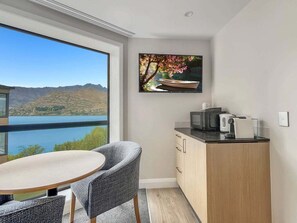 A modern room with a dining area, a kitchen, and a large window offering a view of a lake and mountains. - Lake Wakatipu Stay | Close to Town (Queenstown)