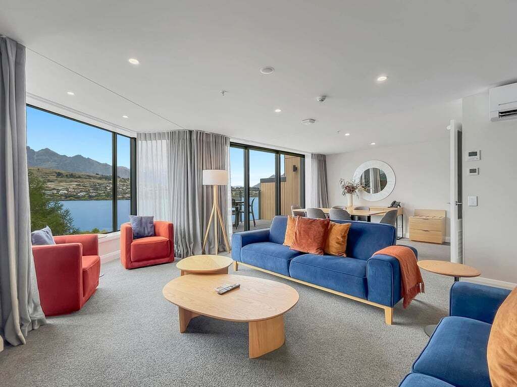 Una habitación de hotel moderna con un ventanal grande, un conjunto de sofás, una mesita de centro y una lámpara.