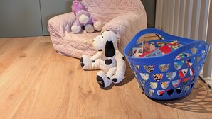 A room with a wooden floor, a pink quilted chair, a stuffed dog, a purple toy, and a blue magazine basket. - Cozy 2-room apartment with a whirlpool tub (Vaugneray)