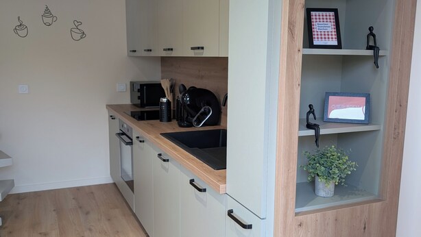 A modern kitchen with light-colored cabinets, a wooden countertop, and a built-in shelf with decorative items. - Cozy 2-room apartment with a whirlpool tub (Vaugneray)