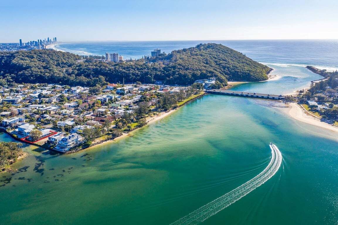An aerial view of a coastal town with a bridge connecting two land masses, a marina, and a clear view of the ocean.