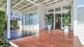 A covered outdoor area with a wooden deck, potted plants, and a modern building entrance. - Luxury Waterfront Stay at Tallebudgera Creek (Gold Coast)