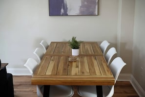 Ein Holzesstisch mit weißen Stühlen, ein kleiner Topfpflanze und ein gerahmtes Kunstwerk an der Wand.