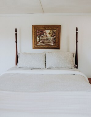 Ein Schlafzimmer mit einem Himmelbett, einem gerahmten Bild an der Wand und einer schlichten weißen Decke.