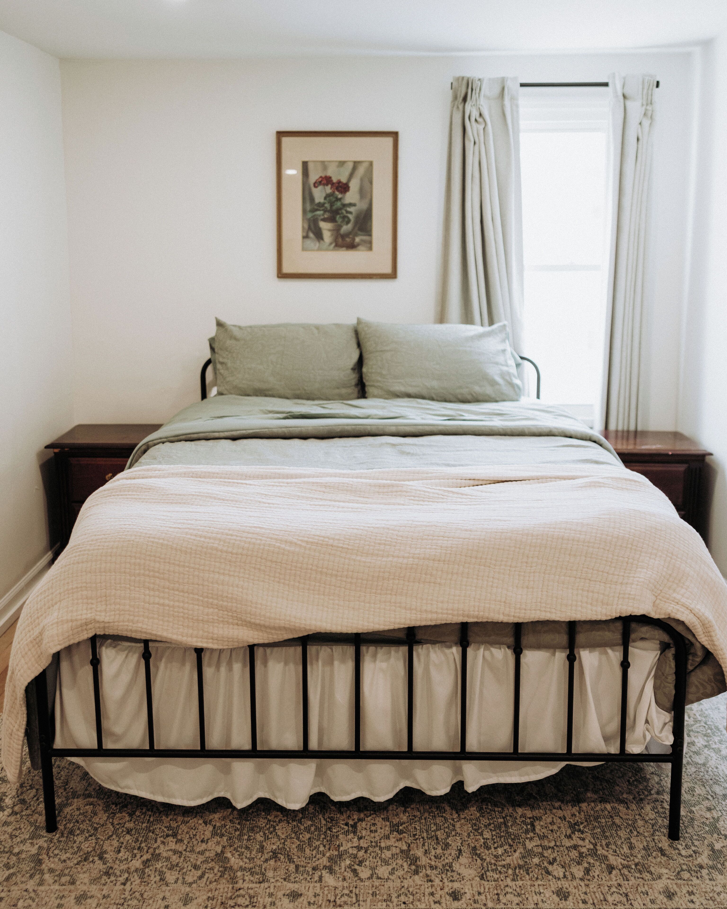 A bedroom with a bed, a nightstand, a framed picture on the wall, and a window with curtains.