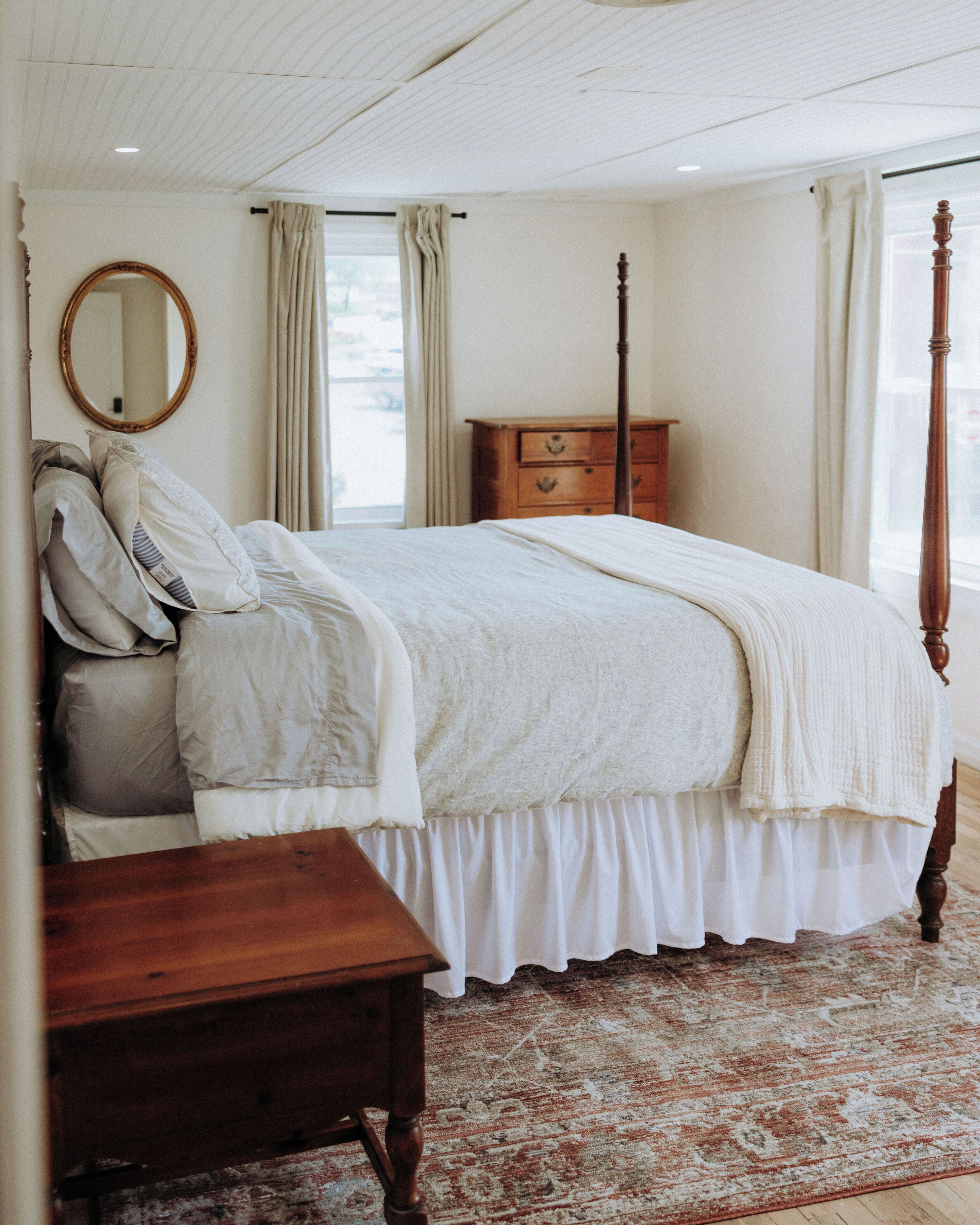 Une chambre à coucher avec un lit à baldaquin, une commode en bois, un miroir et un tapis à motifs.