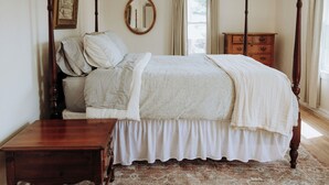 Un dormitorio con cama con dosel, cómoda de madera, mesita de noche y un espejo en la pared.