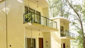 A two-story building with a balcony on the upper floor, surrounded by greenery.
