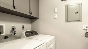 Ett tvättrum med en tvättmaskin och en torktumlare som man matar in tvätten i framifrån, en kontrollpanel och en elcentral på väggen.