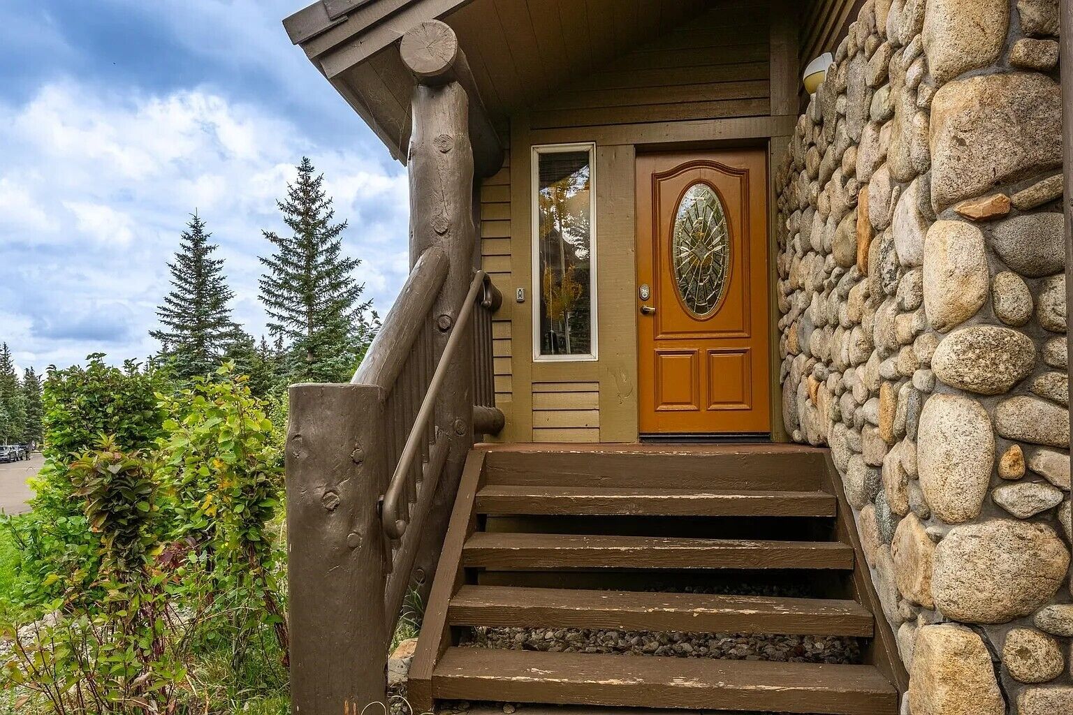 Un escalier en bois mène à une entrée dans un mur de pierre, qui est dotée d’une porte en bois et d’une fenêtre.
