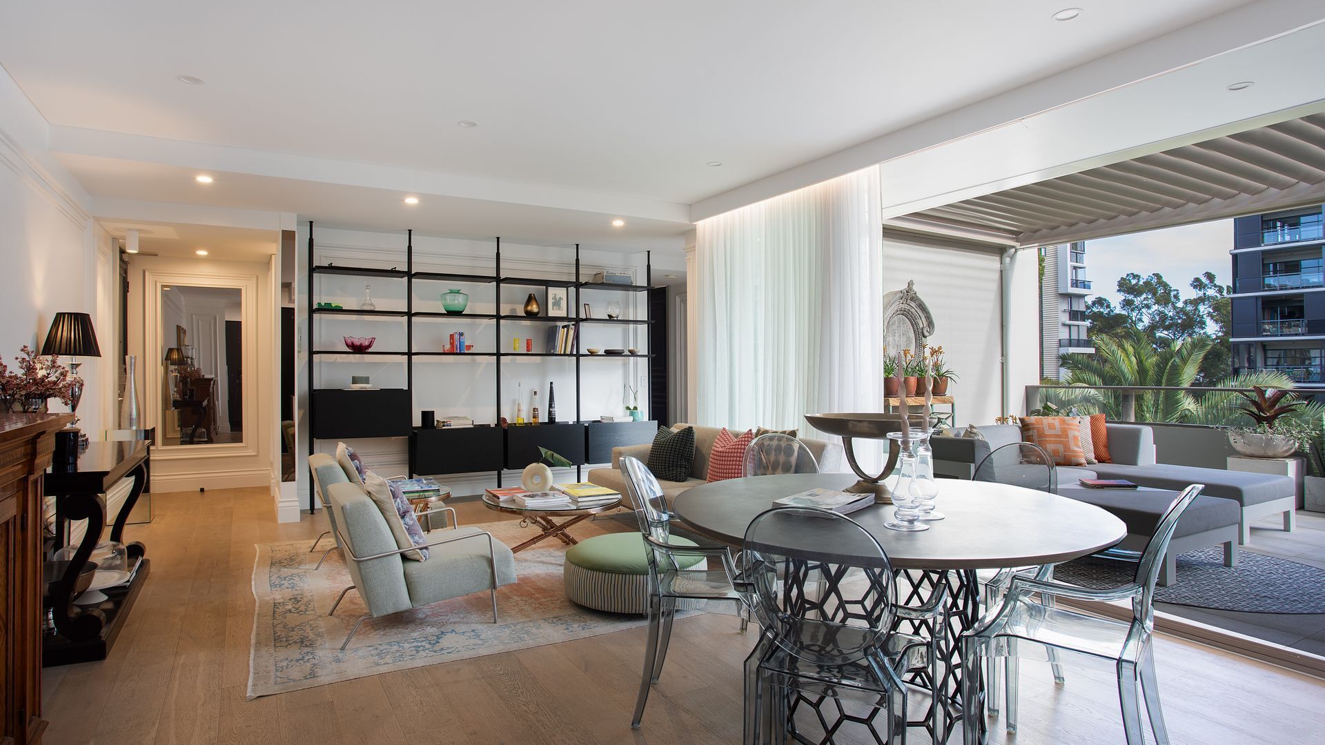 A modern living room with a dining area, a bookshelf, and a view of the outdoors.