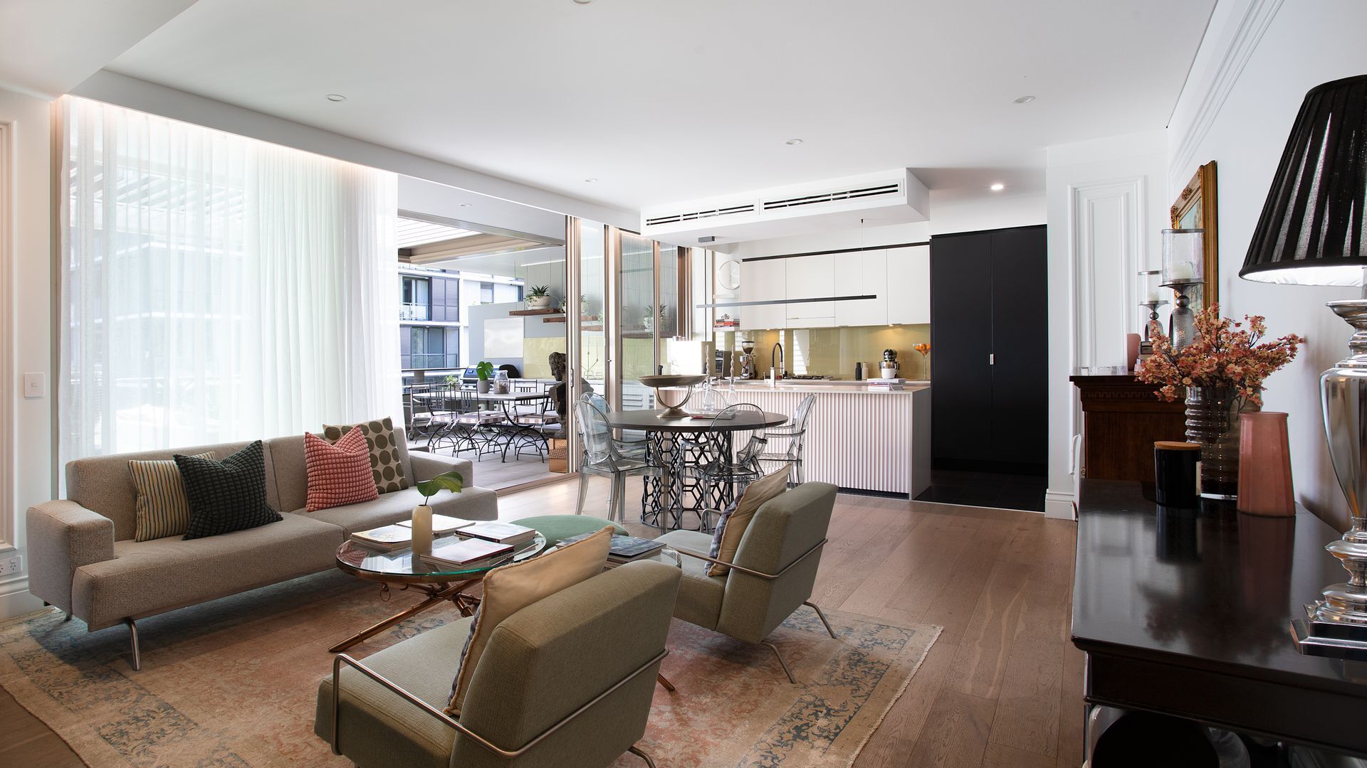 A modern living room with a sofa, chairs, a coffee table, and a dining area with a kitchen in the background.