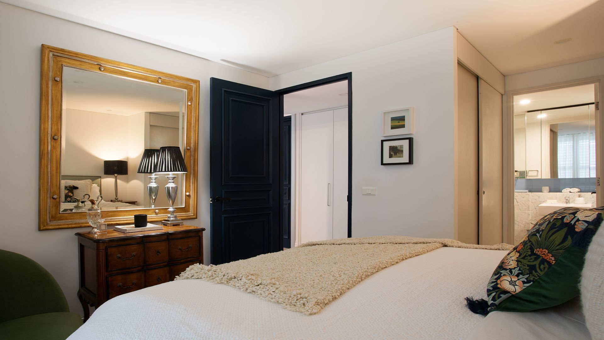 Une chambre à coucher comprenant un lit, une commode, un miroir et une porte donnant sur une autre pièce.