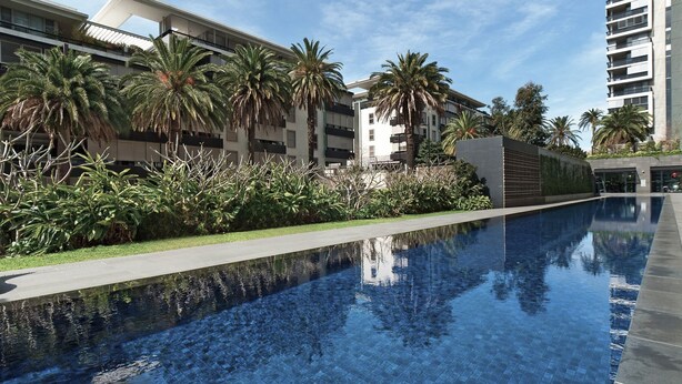 A swimming pool with a clear blue water surface, surrounded by lush greenery and modern buildings. - Alexandra Breeze, Camperdown (Camperdown)