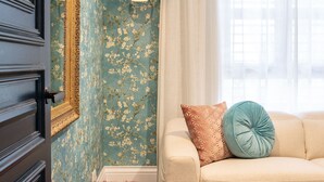 A room with a floral wallpaper, a beige sofa with patterned cushions, and a window with sheer curtains. - Alexandra Breeze, Camperdown (Camperdown)