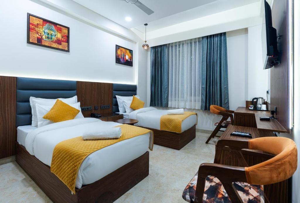 Quarto de hotel com duas camas, uma escrivaninha, uma cadeira e uma televisão.