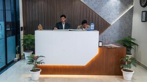 Een receptiebalie met twee personen erachter, omringd door potplanten.