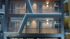 Een meerlaags hotel met een modern ontwerp, met een opvallend 'Hotel Palash' bord, balkons en een groen tapijt op de entree.