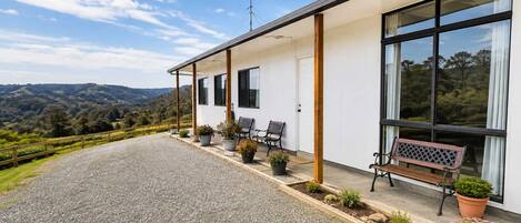 A modern building with a covered porch, outdoor seating, and a gravel driveway.