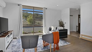 En moderne stue med et stort vindue, et fladskærms-tv, en sofa, to lænestole og et lille bord.