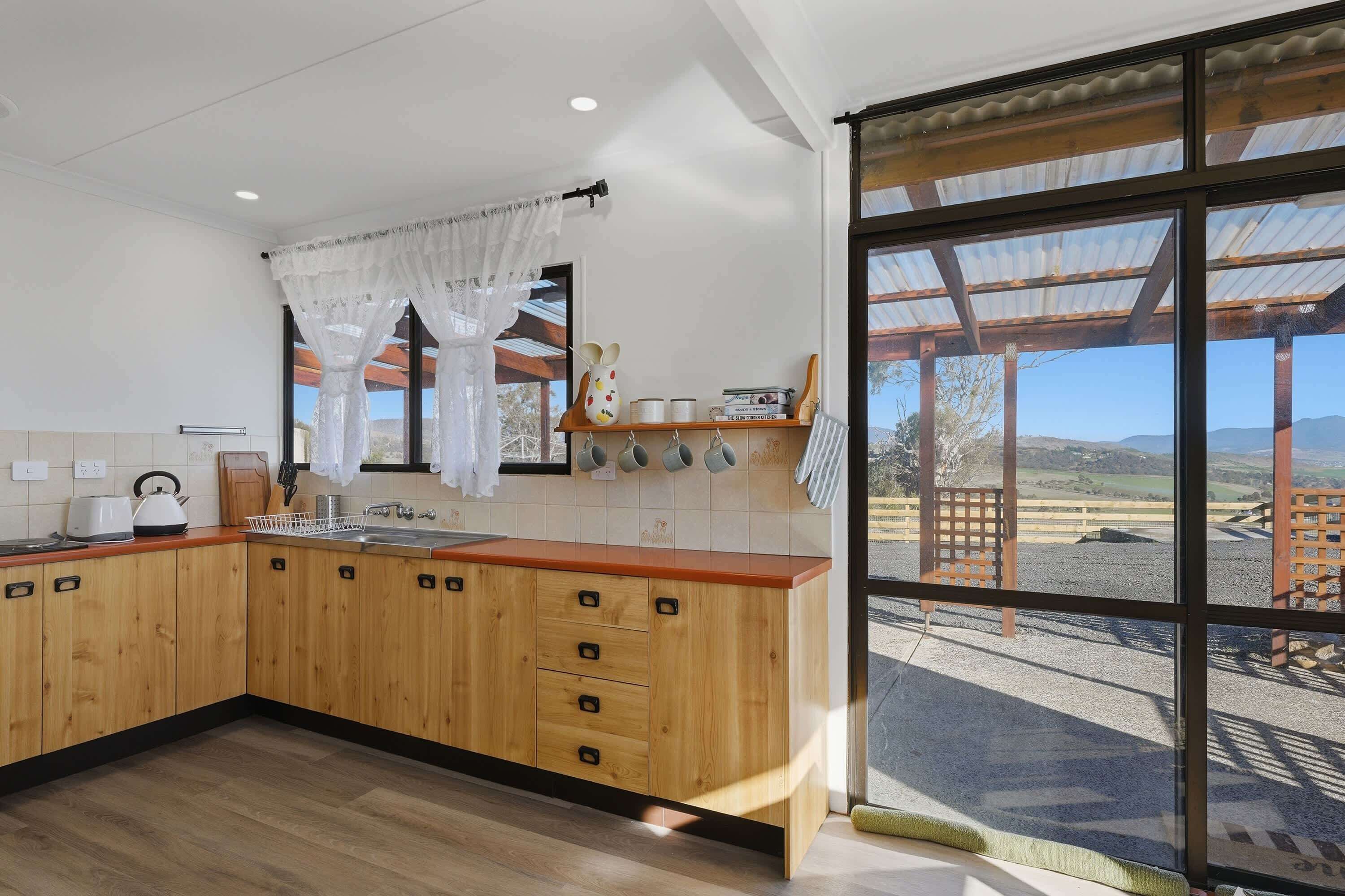 Una cocina moderna con armarios de madera, un lavamanos de acero inoxidable y un amplio ventanal con vistas al campo.