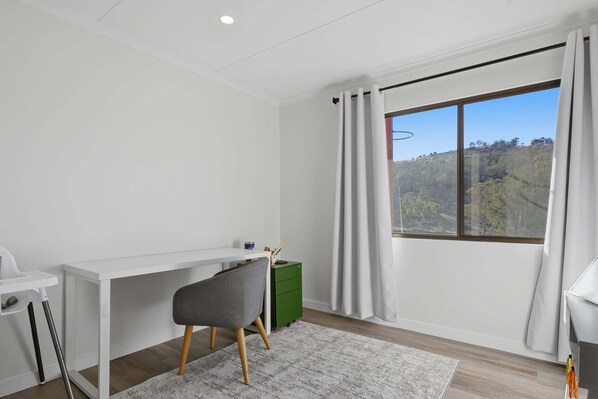 A modern room with a white desk, a grey chair, a green cabinet, and a large window with curtains.