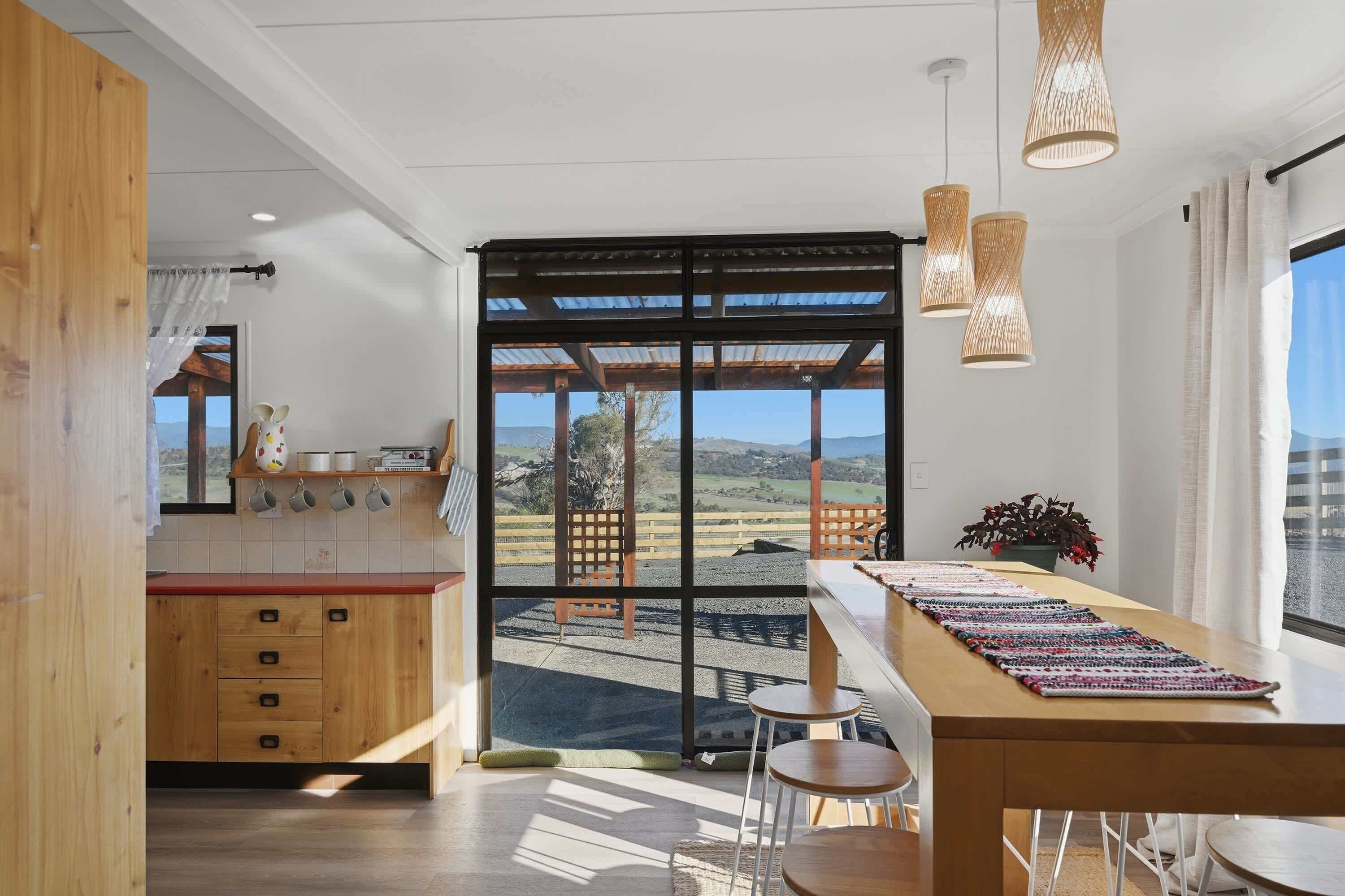 A modern kitchen with a large window, wooden cabinets, and a view of a rural landscape.