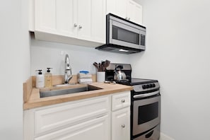 Une cuisine de taille réduite avec des meubles blancs, un four à micro-ondes en acier inoxydable, une cuisinière et un évier.