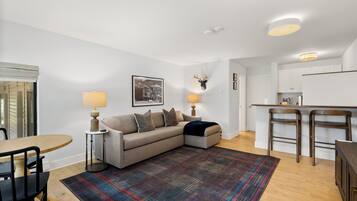 A modern living room with a sofa, a dining table, and a kitchen area.